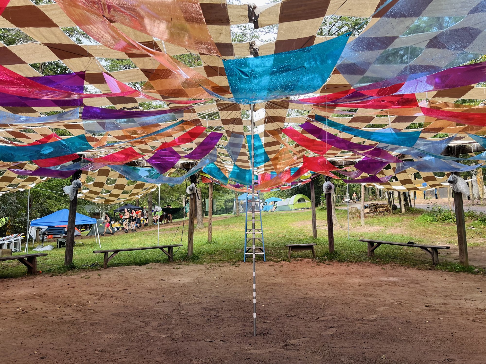 The vinyl quilt canopy spread over the empty drum circle, tents and trees beyond