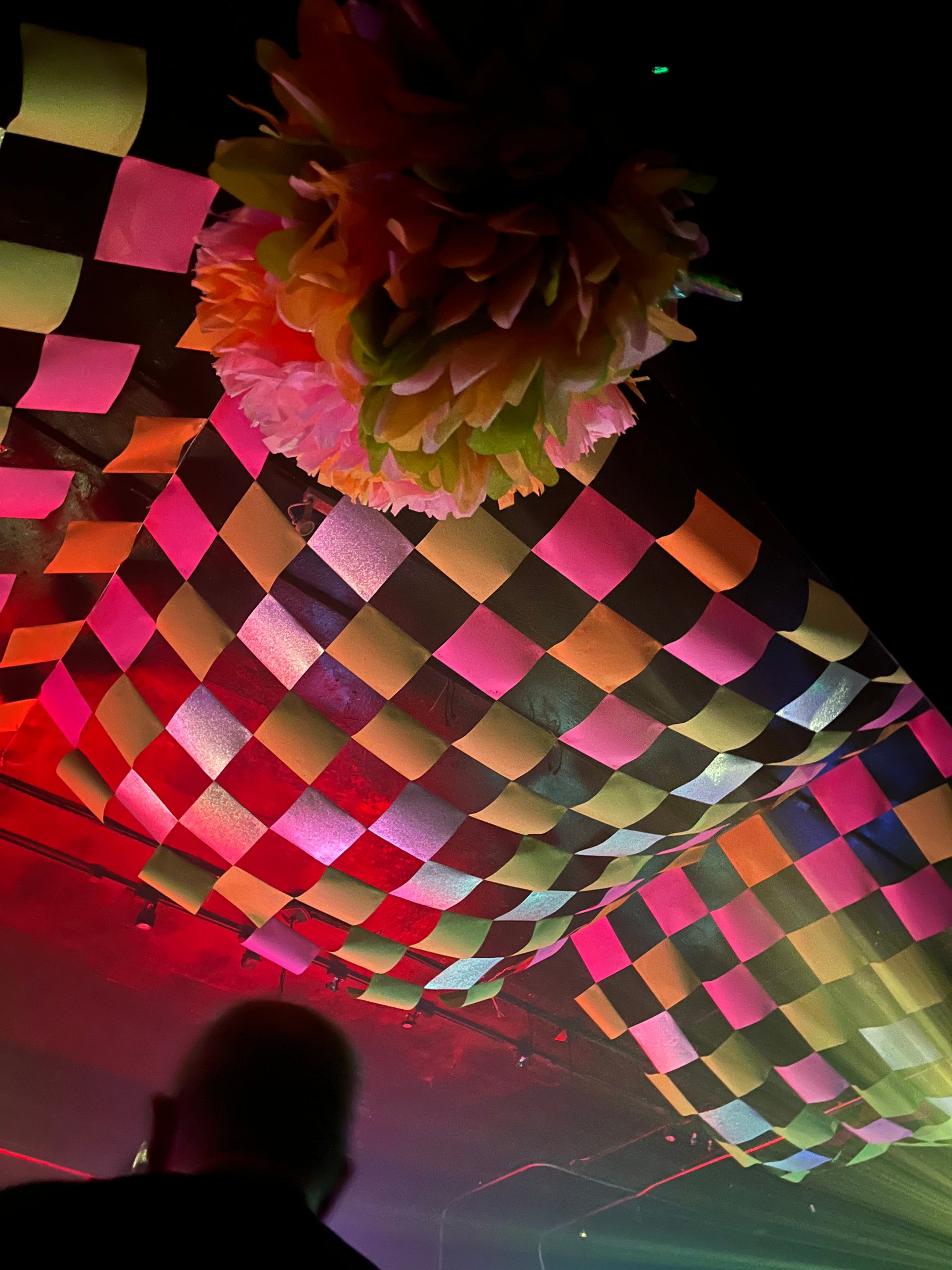 Looking up at the multicolored checkered canopy beneath a tissue-paper pompom